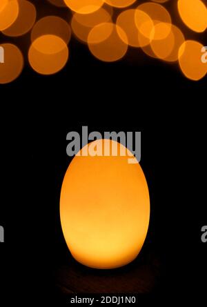 Shining Golden Yellow Egg Shaped Table Lamp with Bokeh Light on Black Background Stock Photo