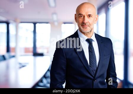 Portrait shot of smiling businessman wearing suit and tie while standing in the conference room. Stock Photo