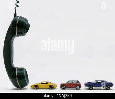 Three small cars waiting in front of a huge telephone handset, copy-space. Stock Photo