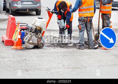 Road workers in reflective clothing on a fenced-in section of road repairing the roadway using a hand-held road tool. Copy space. Stock Photo