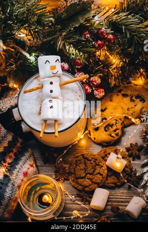 Holiday food white cup with hot chocolate cocoa snowman marshmallows. homemade sweet cookie, cinnamon stick fir xmas tree warm garland lights. Happy N Stock Photo