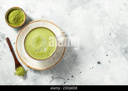 Matcha green tea latte in a cup with cream on a light concrete background. Top view with copy space Stock Photo