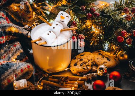 Holiday food white mug with hot chocolate cocoa snowman marshmallows. homemade sweet cookie, cinnamon sticks fir xmas tree branches with warm garland Stock Photo