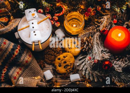 Christmas food white cup with hot chocolate snowman marshmallows. homemade cookie, cinnamon sticks fir xmas tree branches with warm garland lights. Ne Stock Photo