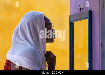 African Ghana woman standing in front of a mirror with a white shawl covering her hair Stock Photo