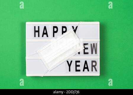 Lightbox with text HAPPY NEW YEAR with medical mask on green background. New year celebration during coronavirus pandemic. Top view Stock Photo