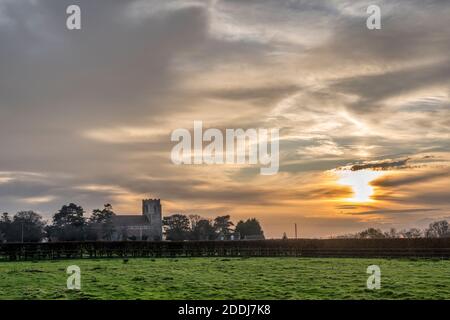 Sun setting behind the Church of St Peter, Wolferton across fields on the Sandringham Estate in Norfolk Stock Photo