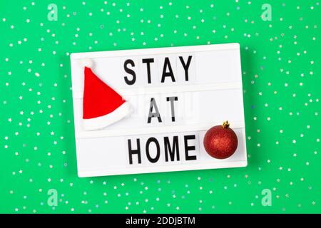Light box with text STAY AT HOME and Christmas decoration on green background with gold glitter stars. Top view Stock Photo