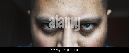Evil look of angry or tired male with bags or black circles under spooky eyes, close up portrait. Horror creepy demon or bad negative person looks at camera. Stock Photo