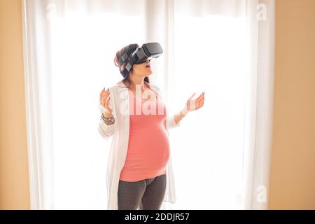 Young beautiful pregnant woman wearing  using virtual reality glasses at home. Connection, technology, new generation and progress concept Stock Photo