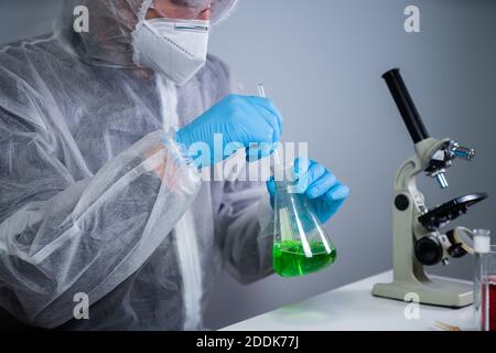 Scientist shaking green fluid in beaker. Young laboratory assistant making test or research in lab. Technician testing chemistry lab experiment and Stock Photo