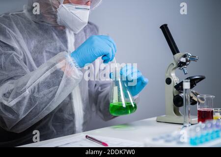 Scientist shaking green fluid in beaker. Young laboratory assistant making test or research in lab. Technician testing chemistry lab experiment and Stock Photo
