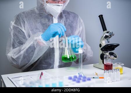 Scientist shaking green fluid in beaker. Young laboratory assistant making test or research in lab. Technician testing chemistry lab experiment and Stock Photo