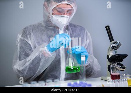 Scientist shaking green fluid in beaker. Young laboratory assistant making test or research in lab. Technician testing chemistry lab experiment and Stock Photo