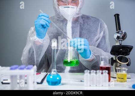 Scientist shaking green fluid in beaker. Young laboratory assistant making test or research in lab. Technician testing chemistry lab experiment and Stock Photo