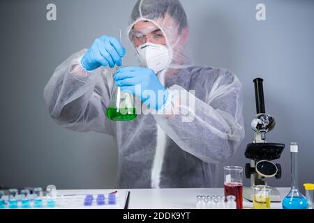 Scientist shaking green fluid in beaker. Young laboratory assistant making test or research in lab. Technician testing chemistry lab experiment and Stock Photo