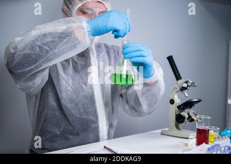 Scientist shaking green fluid in beaker. Young laboratory assistant making test or research in lab. Technician testing chemistry lab experiment and Stock Photo