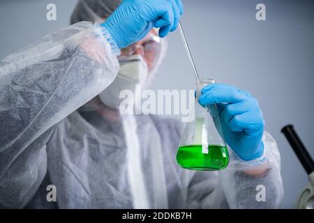 Scientist shaking green fluid in beaker. Young laboratory assistant making test or research in lab. Technician testing chemistry lab experiment and Stock Photo
