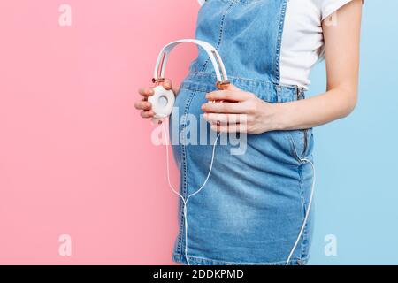 Close - up of a pregnant woman's belly holding headphones with music near her belly, on a pink and blue background Stock Photo