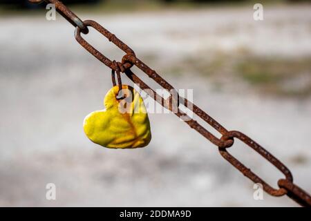 a yellow heart hanging on a rusty chain Stock Photo