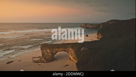 Romantic sun rise at dark rock of Bawana sand beach, sea gulf coastline. Relax seascape sunrise at wavy ocean cliff coast of Sumba Island, Indonesia aerial view. Cinematic soft light drone shot Stock Photo