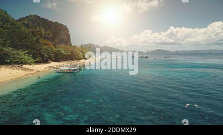 Sun sand beach at green mountain island with passenger boats and resting travelers aerial panorama view. Tropic paradise isle landscape: greenery exotic plants and trees. People admire tropical cruise Stock Photo