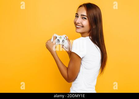 Happy woman smiles at camera and holds joystick in hand, on yellow background Stock Photo