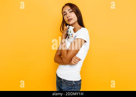 Happy woman smiles at camera and holds joystick in hand, on yellow background Stock Photo
