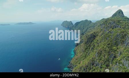 Aerial view of mountain island with green tropic forest. Epic landscape of ocean bay greenery cliff shore at sand beach. Boats at sea gulf with turquoise seascape of Palawan Island, Philippines, Asia Stock Photo