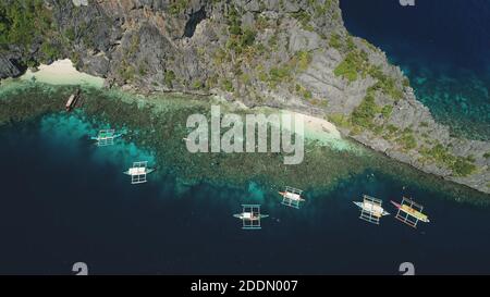 Boats at cliff ocean shore with sand beach at coast aerial view. Nature beauty of tropic mountainous islet in top down drone shot. Amazing seascape with vessels at rock shoreline. Cinematic soft light Stock Photo