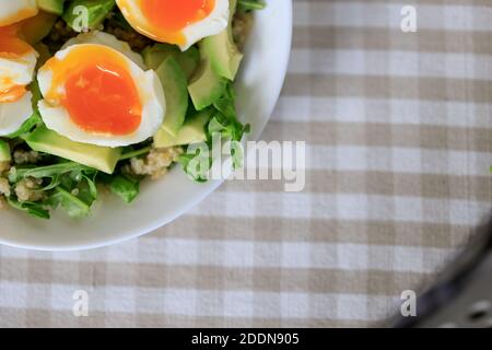 Salad with avocado, quinoa, arugula, soft-boiled eggs on a white plate. Close-up, top view. Healthy, healthy and healthy breakfast concept. Stock Photo