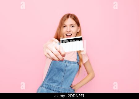 Portrait of a happy young woman in casual clothes holding a credit card isolated on a pink background Stock Photo