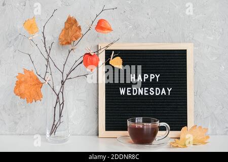 Happy Wednesday text on black letter board and bouquet of branches with yellow leaves on clothespins in vase on table Template for postcard, greeting Stock Photo