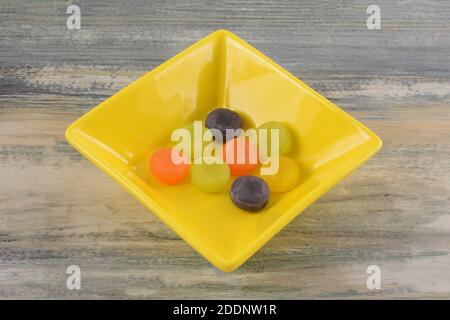 Round fruit flavored jelly hard candies in yellow candy dish on table Stock Photo