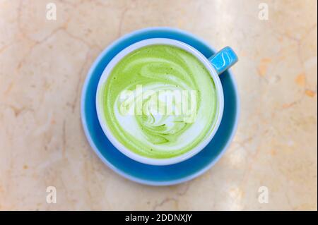 matcha green tea latte with a pattern of milk foam in a blue ceramic cup on the table Stock Photo