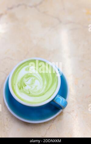matcha green tea latte with a pattern of milk foam in a blue ceramic cup on the table. vertical photo Stock Photo
