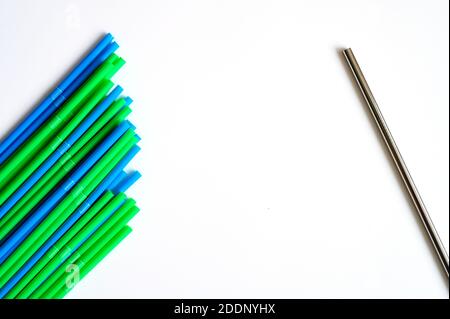 a pile of disposable plastic drinking straws and one reusable stainless steel metal drinking straw on a white background Stock Photo