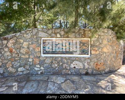 Glass and painting wall art on an outside stone wall. Stone ground and pine trees at the background. Water and wave motif. Stock Photo