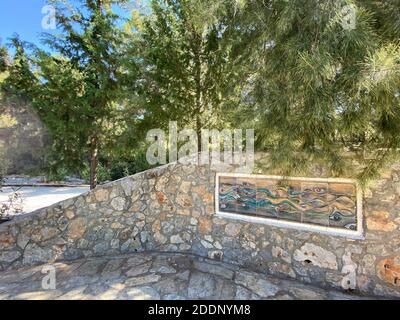 Glass and painting wall art on an outside stone wall. Stone ground and pine trees at the background. Water and wave motif. Stock Photo