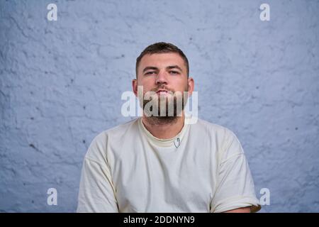 Photo of a bearded young man wearing in a white t-shirt standing on a graffiti wall background. Horizontal mock up. Stock Photo