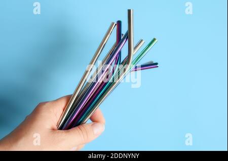 several reusable metal stainless steel drinking straws in female hand on a blue background Stock Photo
