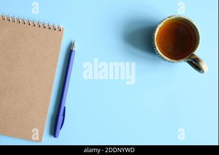 notebook or sketchbook made of craft paper and a pen and tea cup on a blue background. space for text Stock Photo