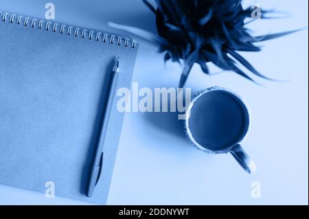 notebook or sketchbook made of craft paper and a pen and tea cup and green plant on a blue background. tinted classic blue color trend 2020 year Stock Photo