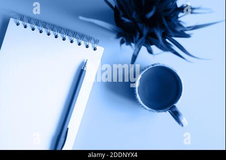 notebook or sketchbook and a pen and tea cup and green plant on a blue background. tinted classic blue color trend 2020 year Stock Photo