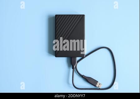 external hard drive black color with connection cable on blue background Stock Photo