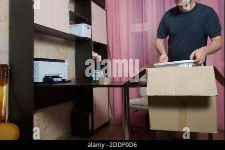The man puts things in a cardboard box. Moving to a new place of residence. Stock Photo
