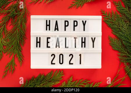 Happy Healthy 2021 year displayed on a white vintage lightbox on bright red background with juniper branches around, flat lay. Stock Photo
