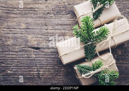 Modern Christmas wrapped presents with natural decor on old wooden background. Three gifts boxes in craft paper with twine and green branches. Seasona Stock Photo