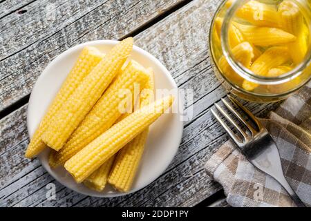 Pickled young baby corn cobs on a plate. Top view. Stock Photo