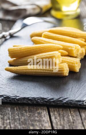 Pickled young baby corn cobs on a black stone cutting board. Stock Photo